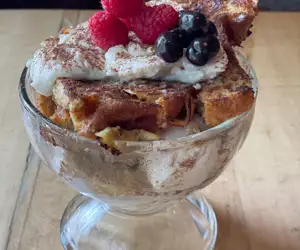 Tiramisu french toast layered in a glass bowl with cream and fresh berries